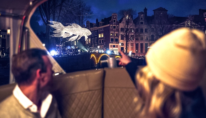 Canal view of illuminated fish sculpture during Amsterdam Light Festival cruise.