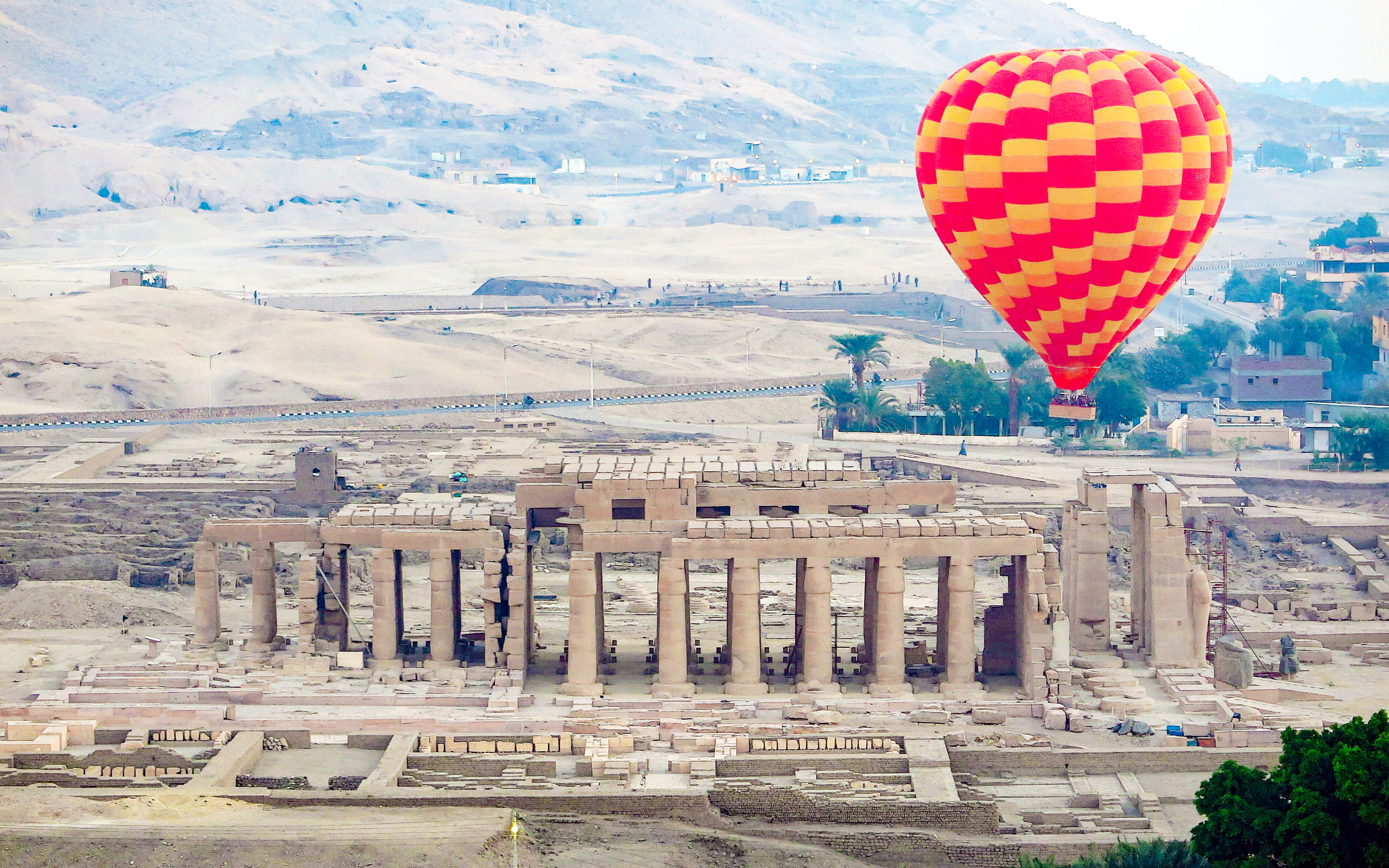 Hot air balloon over Luxor's ancient ruins with desert backdrop.