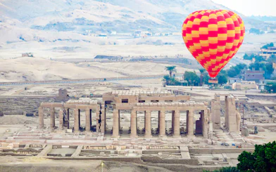 Hot air balloon over Luxor's ancient ruins with desert backdrop.
