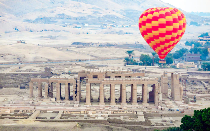 Hot air balloon over Luxor's ancient ruins with desert backdrop.