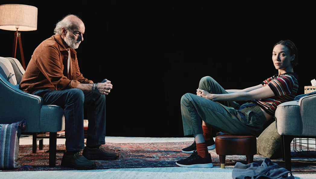 Two people sitting in a dimly lit room, engaged in conversation.