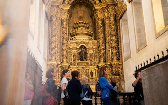 Tourists with guide in Monastery of São Bento da Vitória, Porto, admiring ornate altar.