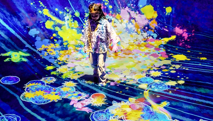Child interacting with colorful digital art installation at Team Lab