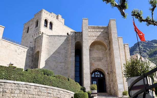 Skanderbeg Museum entrance with stone facade and Albanian flag in Krujë, Albania.