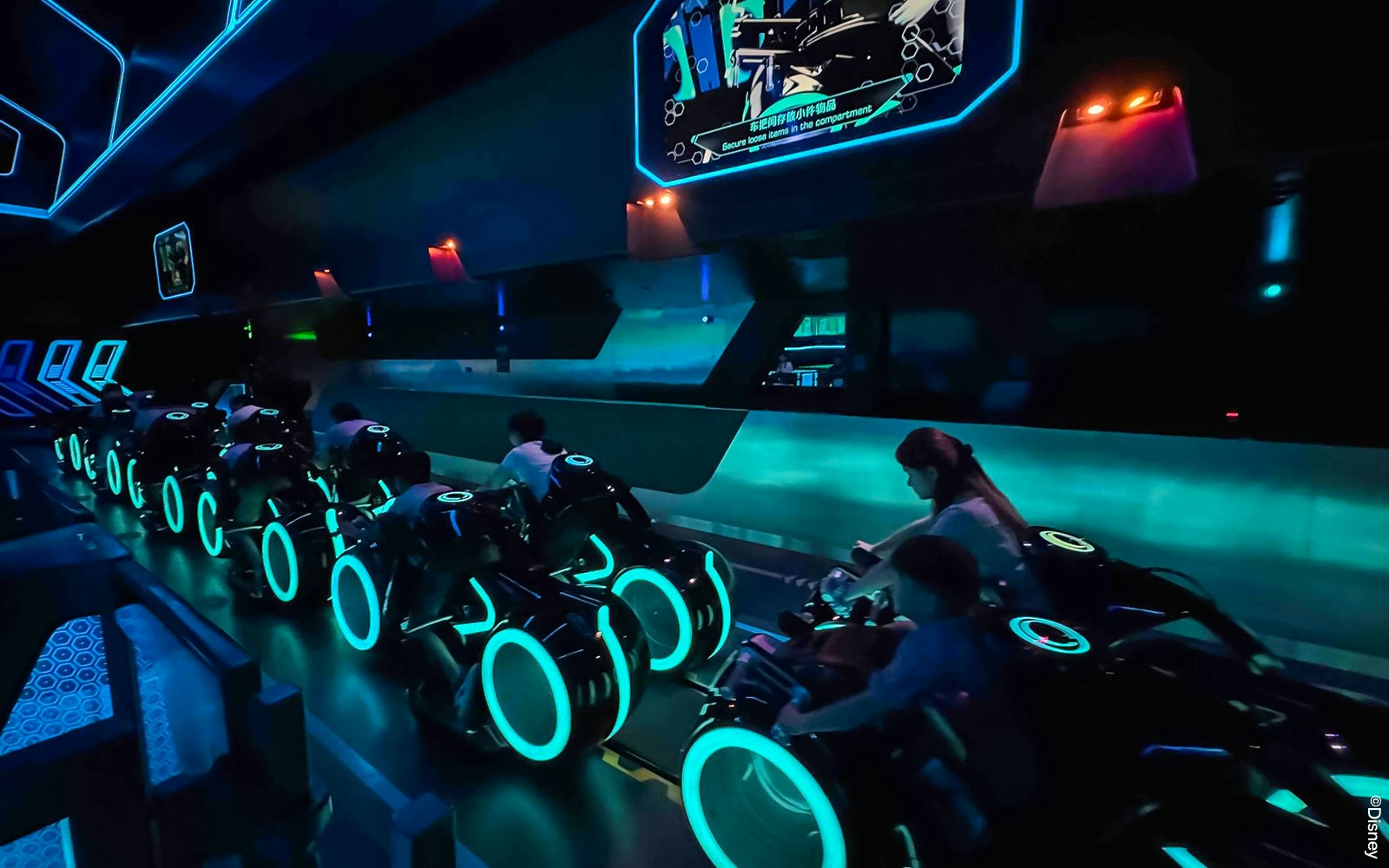 Riders on TRON Lightcycle Power Run attraction in a futuristic, neon-lit setting.