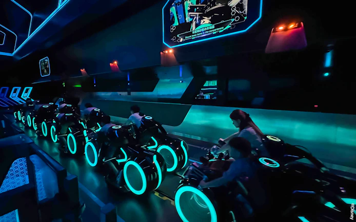 Riders on TRON Lightcycle Power Run attraction in a futuristic, neon-lit setting.