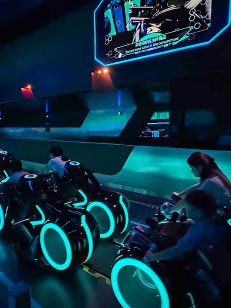 Riders on TRON Lightcycle Power Run attraction in a futuristic, neon-lit setting.
