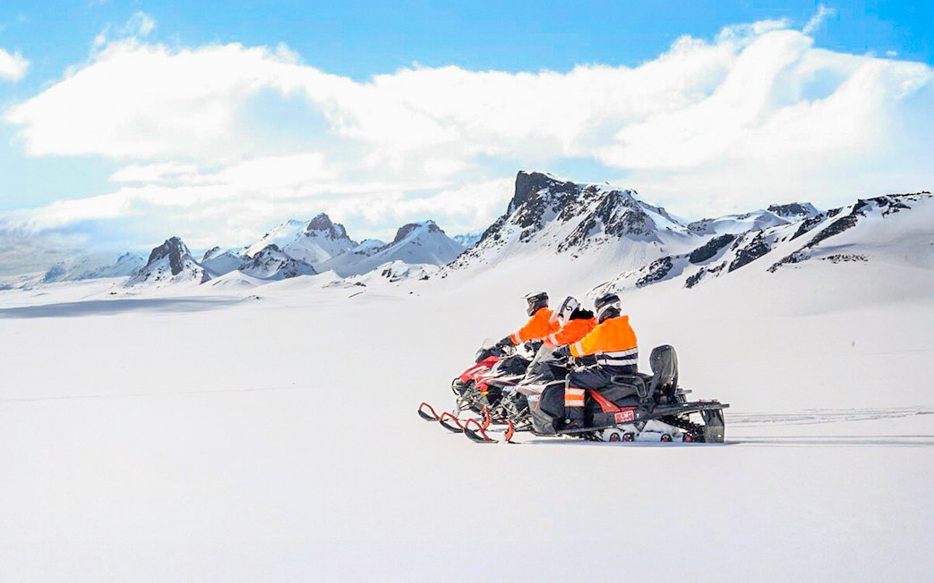 Snowmobile riders on Langjökull Glacier with snowy mountain backdrop.