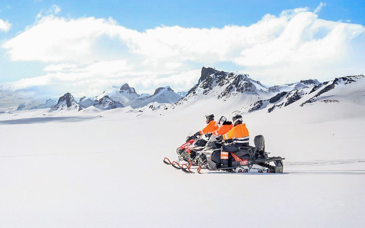 Snowmobile riders on Langjökull Glacier with snowy mountain backdrop.