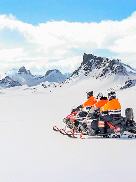 Snowmobile riders on Langjökull Glacier with snowy mountain backdrop.