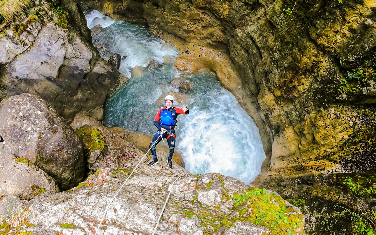 Person rappelling down a rocky canyon with rushing water in Interlaken.
