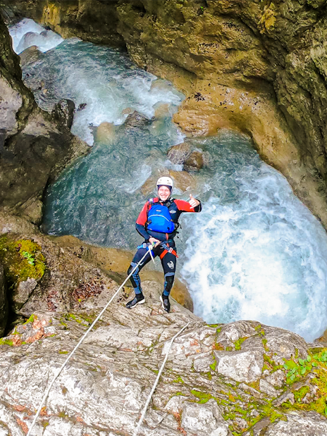 Person rappelling down a rocky canyon with rushing water in Interlaken.