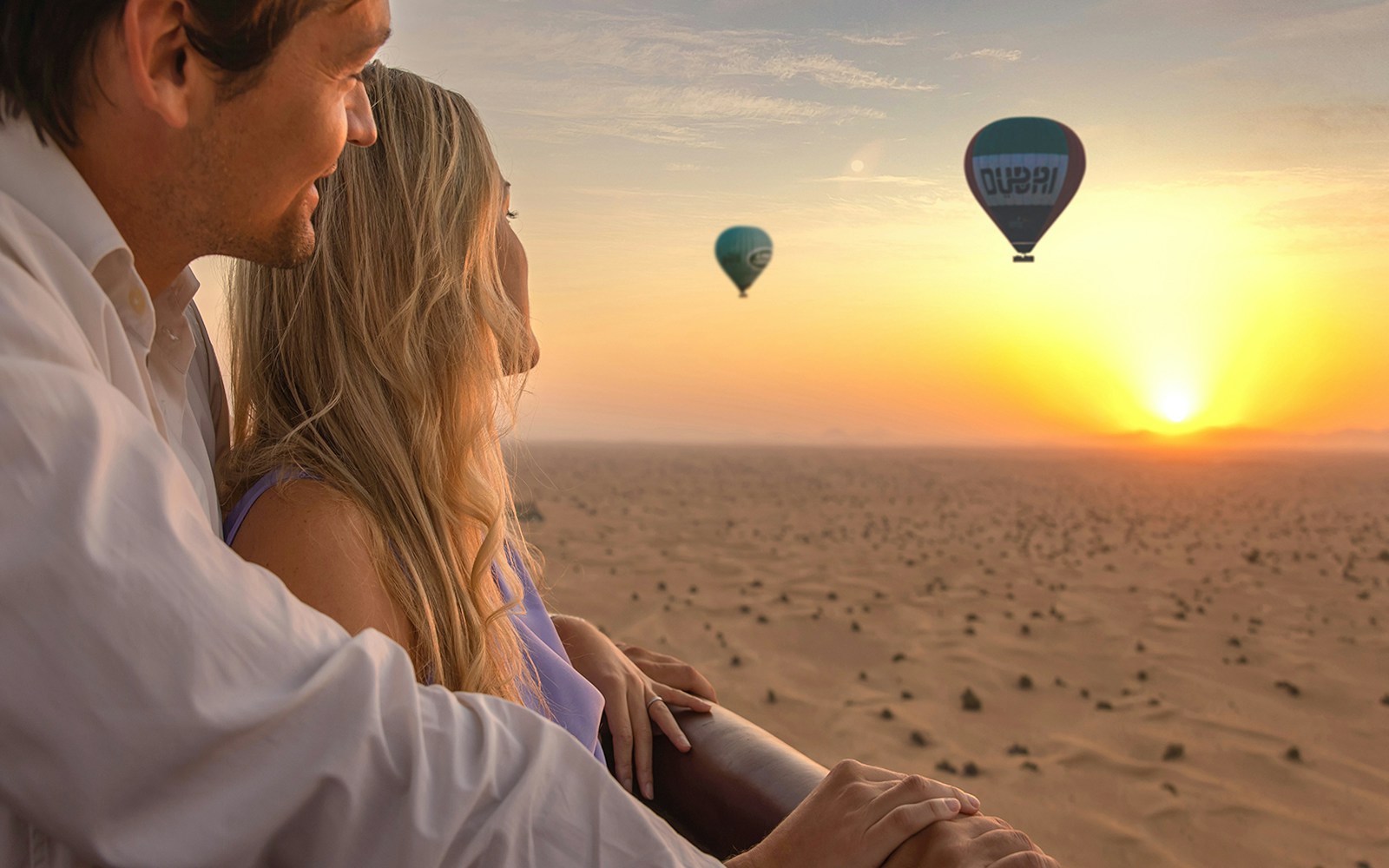 Couple enjoying sunrise from hot air balloon over Dubai desert.