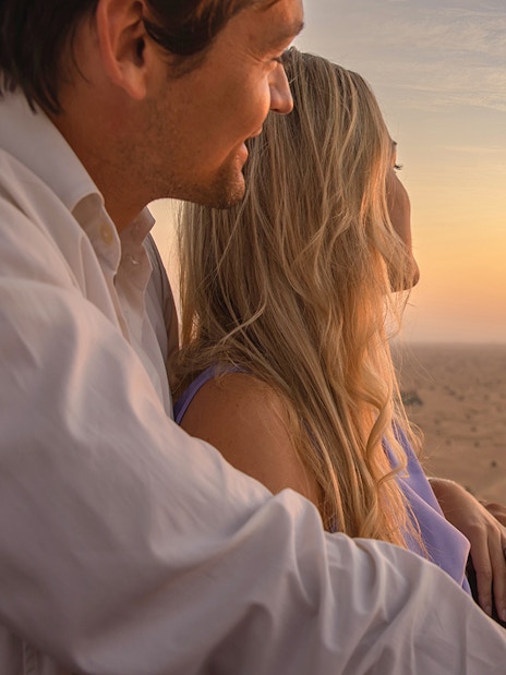 Couple enjoying sunrise from hot air balloon over Dubai desert.