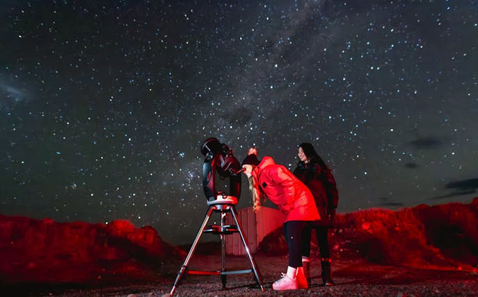 Tourists stargazing with a telescope at The Crater under a starry sky.
