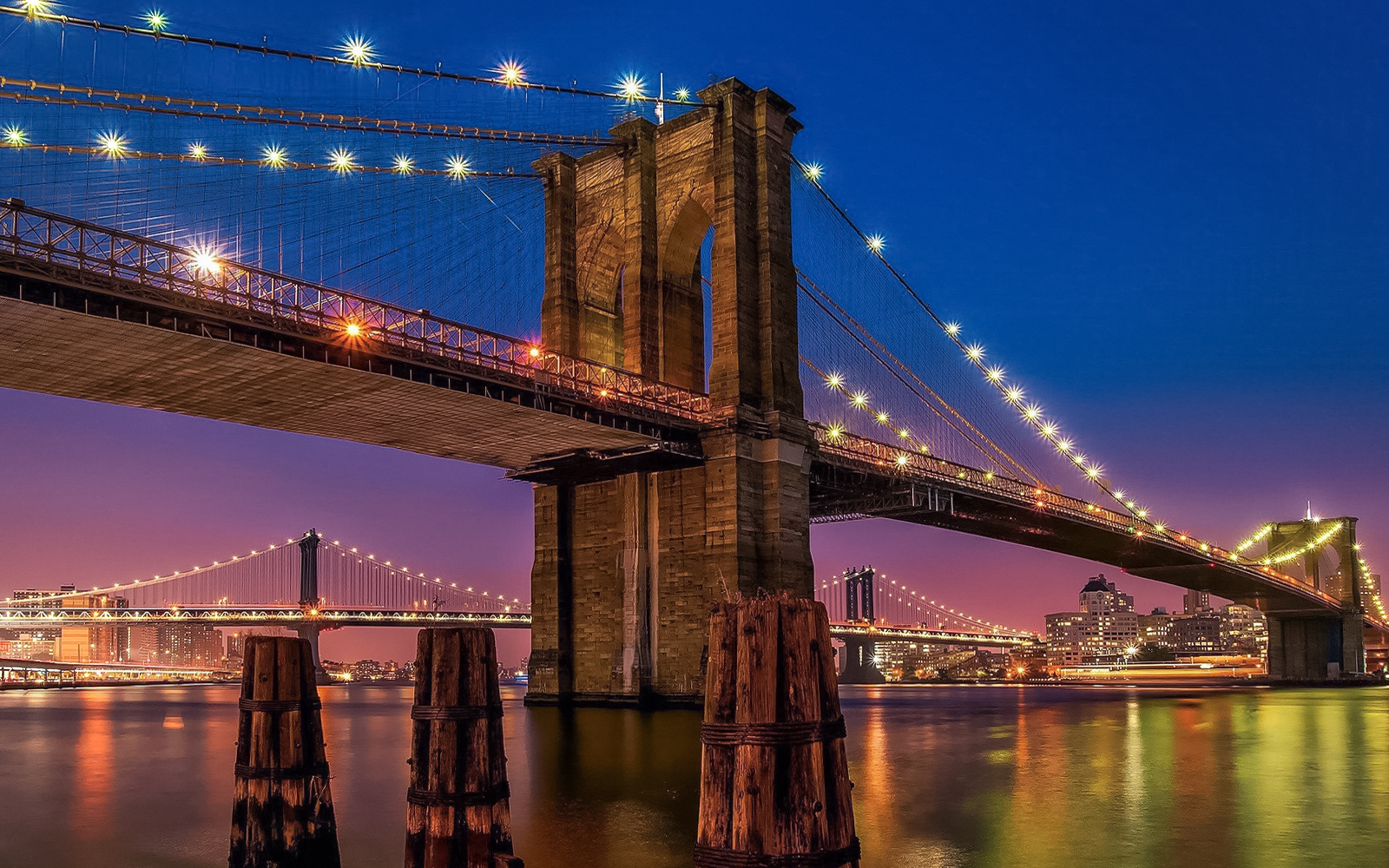 Brooklyn Bridge illuminated at sunset, view from Statue of Liberty & Ellis Island cruise.