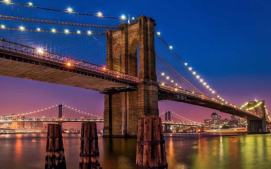 Brooklyn Bridge illuminated at sunset, view from Statue of Liberty & Ellis Island cruise.