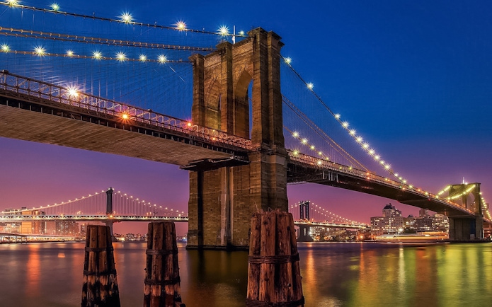 Brooklyn Bridge illuminated at sunset, view from Statue of Liberty & Ellis Island cruise.