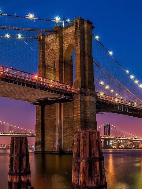 Brooklyn Bridge illuminated at sunset, view from Statue of Liberty & Ellis Island cruise.
