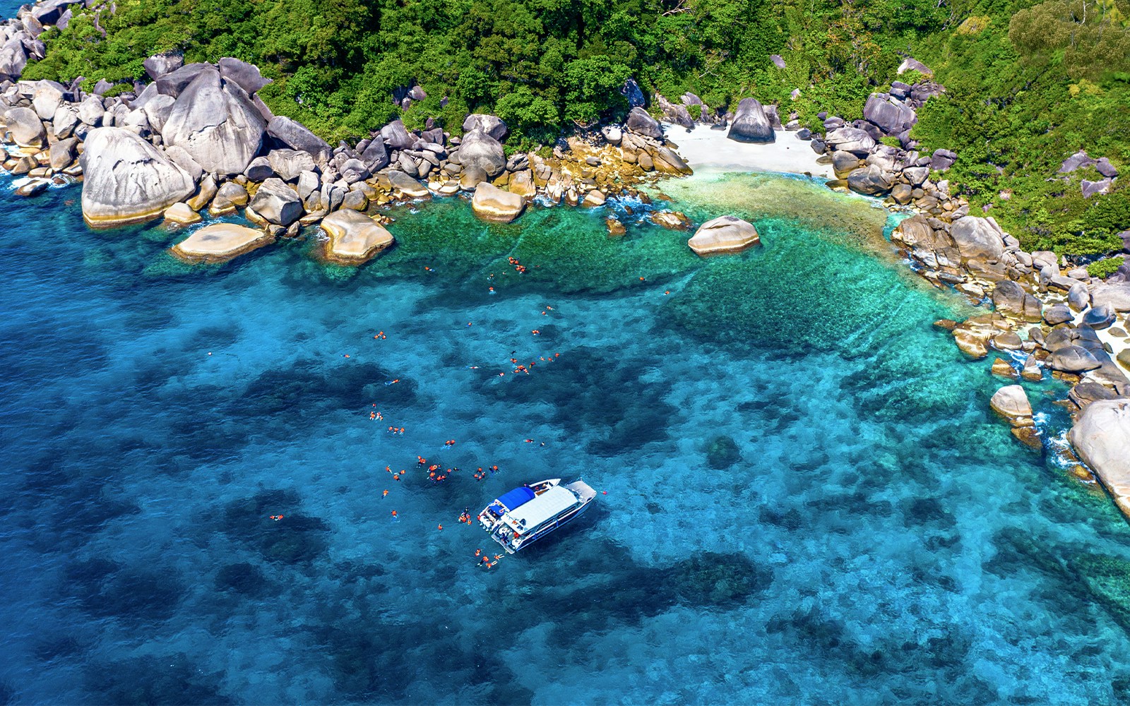 Speedboat near Similan Islands with snorkelers in clear blue water, surrounded by rocky shoreline.