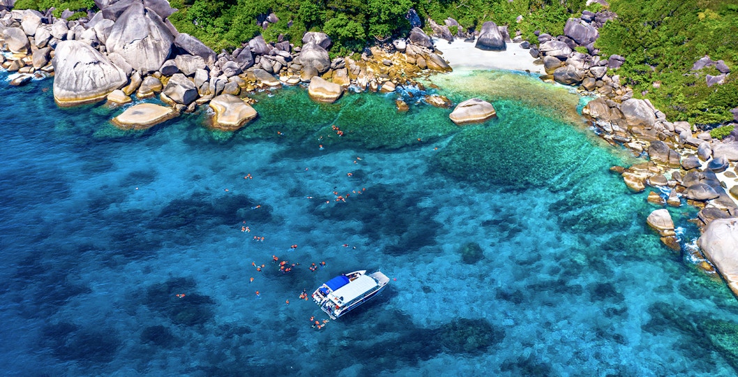 Speedboat near Similan Islands with snorkelers in clear blue water, surrounded by rocky shoreline.