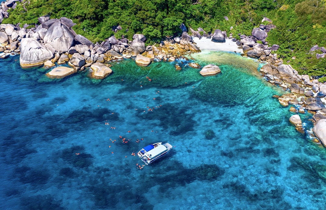 Speedboat near Similan Islands with snorkelers in clear blue water, surrounded by rocky shoreline.