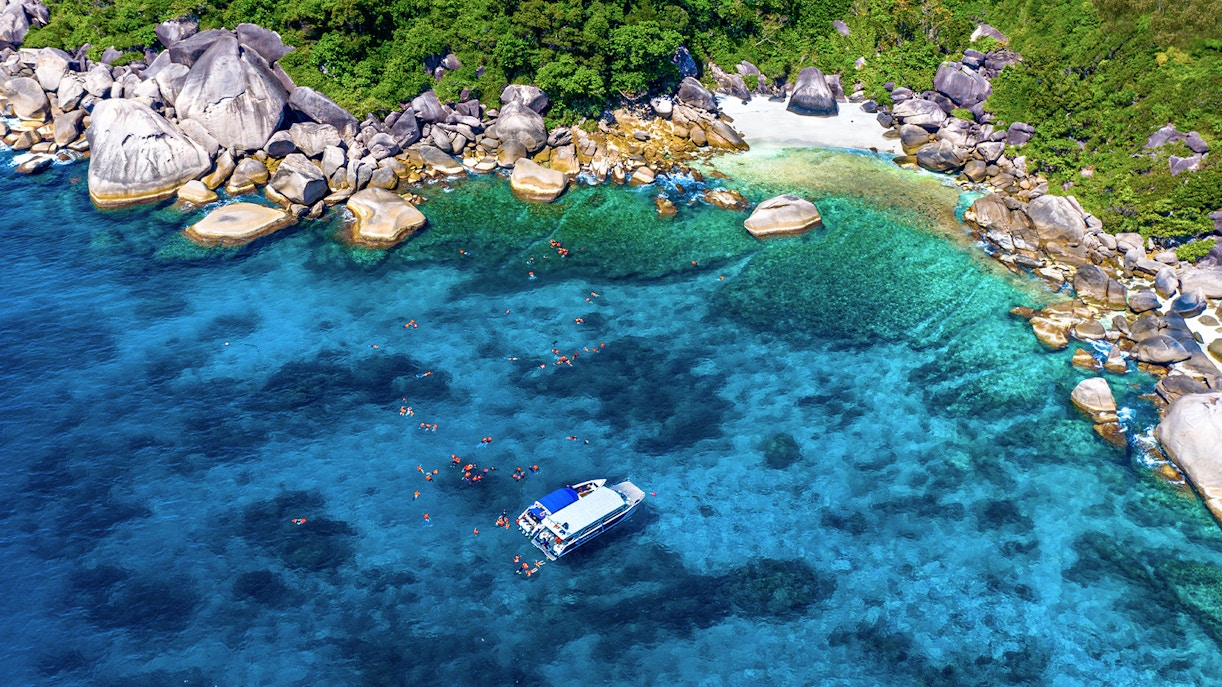 Speedboat near Similan Islands with snorkelers in clear blue water, surrounded by rocky shoreline.