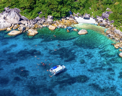 Speedboat near Similan Islands with snorkelers in clear blue water, surrounded by rocky shoreline.