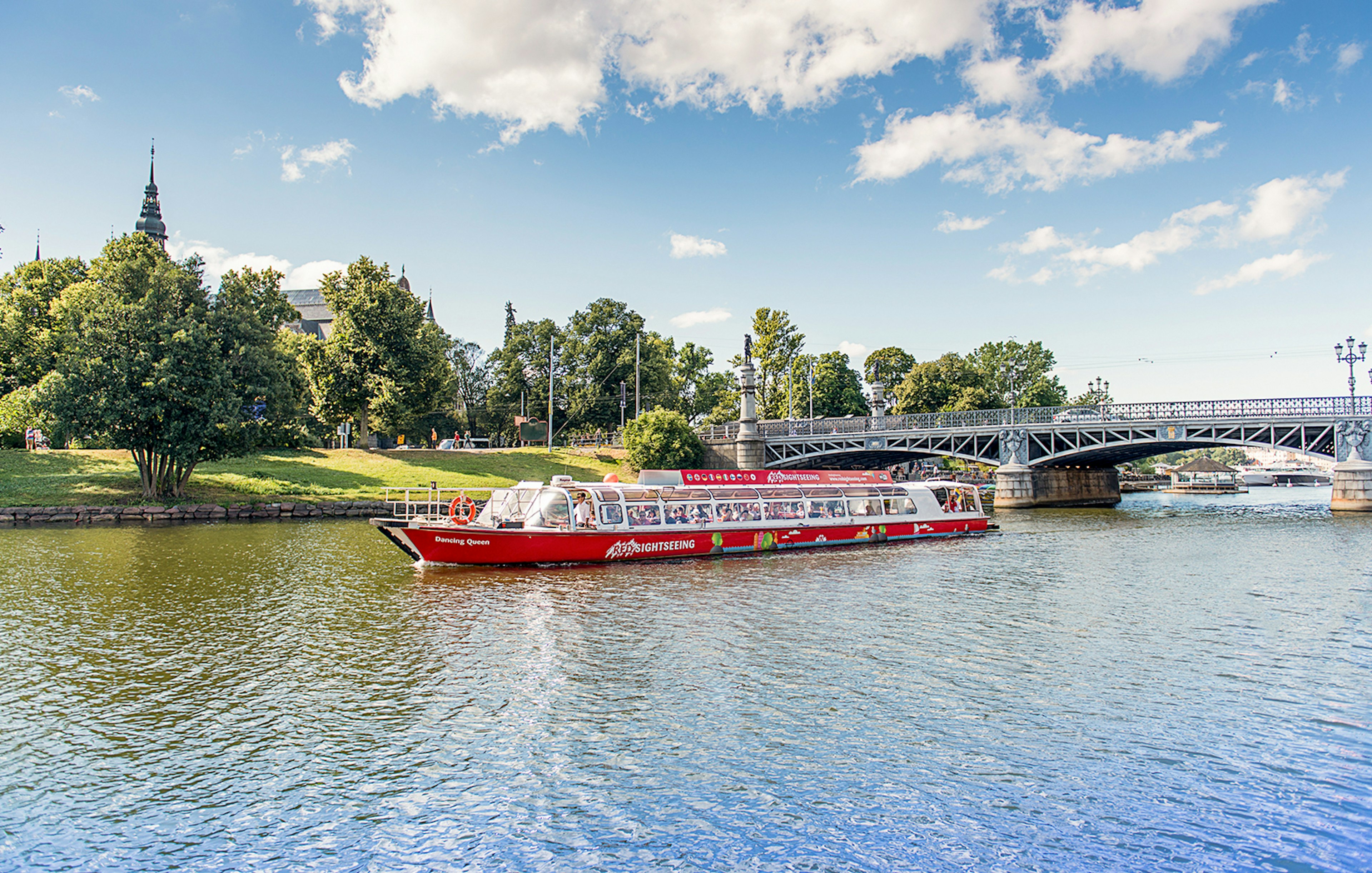 Stockholm sightseeing boat on water near a bridge and greenery.