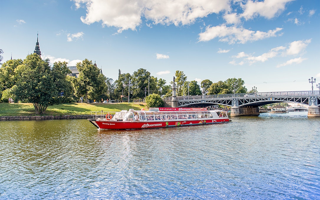 Stockholm sightseeing boat on water near a bridge and greenery.