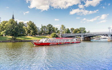 Stockholm sightseeing boat on water near a bridge and greenery.