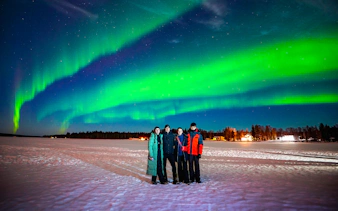 Northern Lights over snowy landscape with family in Rovaniemi, Finland.