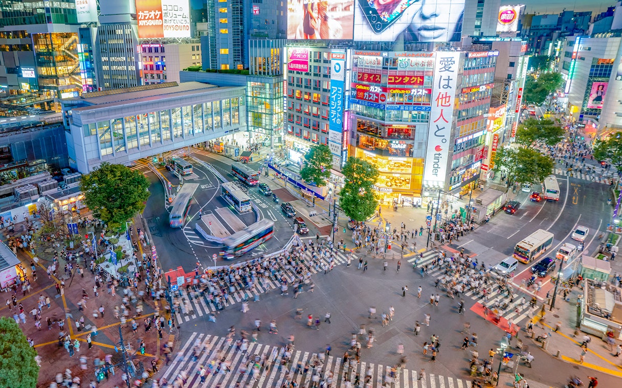 Shibuya Crossing view from Shibuya Sky Deck, Tokyo, with bustling crowds and illuminated buildings.