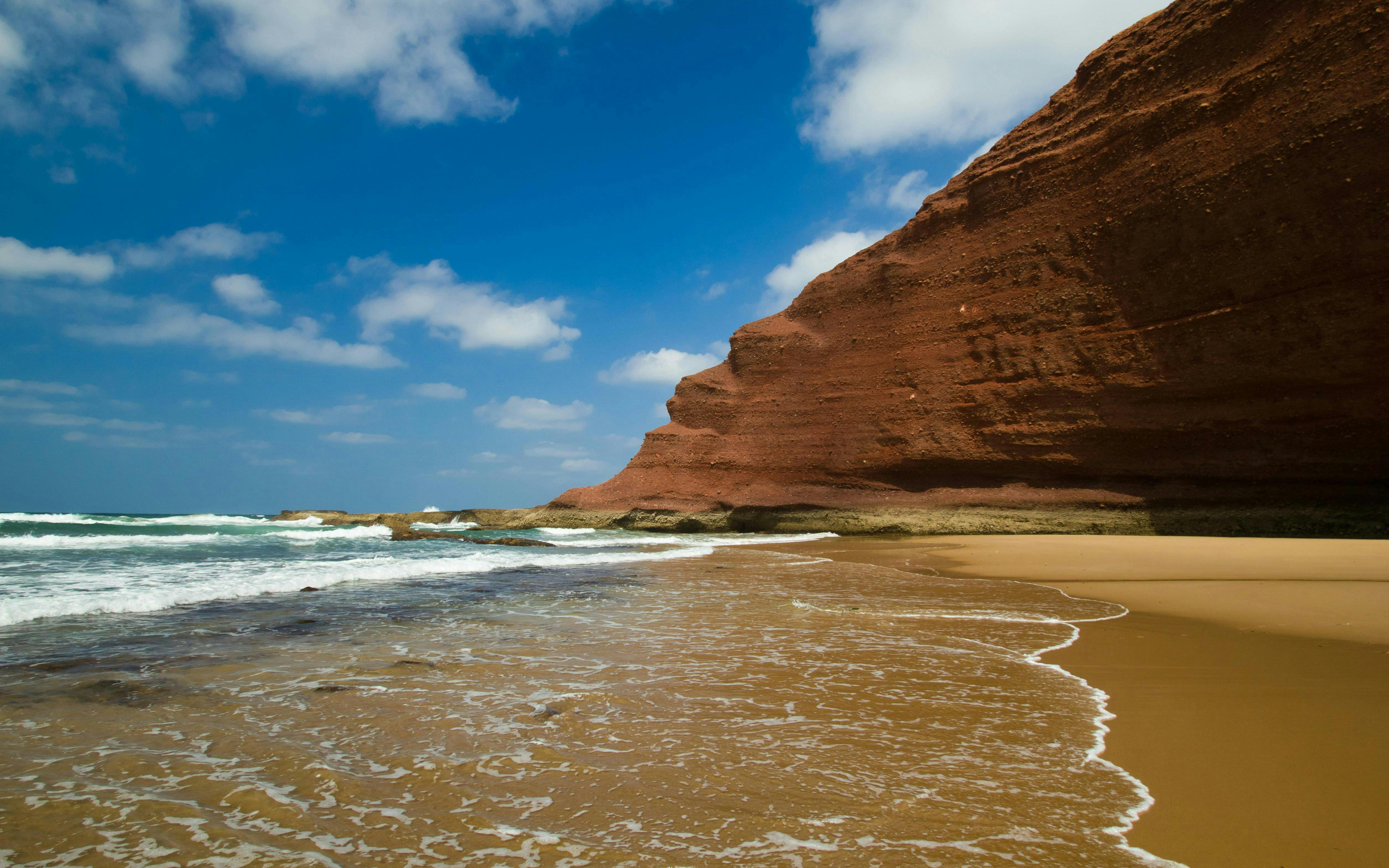 Huge red cliffs on Legzira beach, Morocco, with waves hitting the shore.