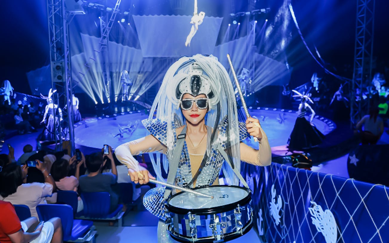 Performer drumming at Aqua Circus Phuket with aerialist in background.