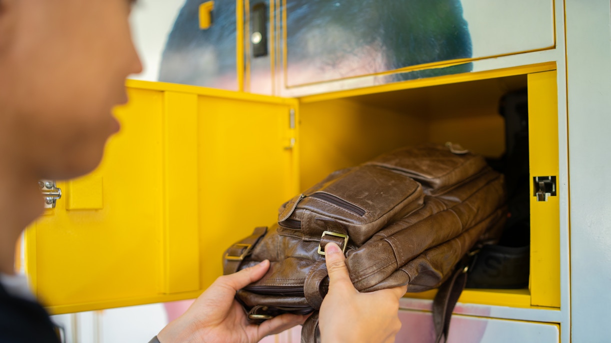 Placing a brown leather bag into a yellow automated parcel terminal locker.