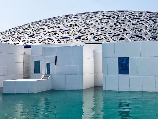 Louvre Abu Dhabi's dome and modern architecture over water.