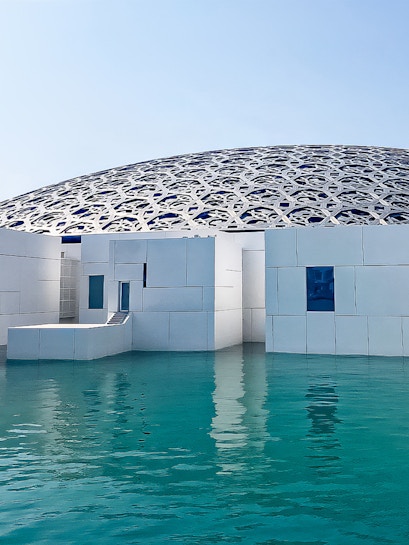 Louvre Abu Dhabi's dome and modern architecture over water.