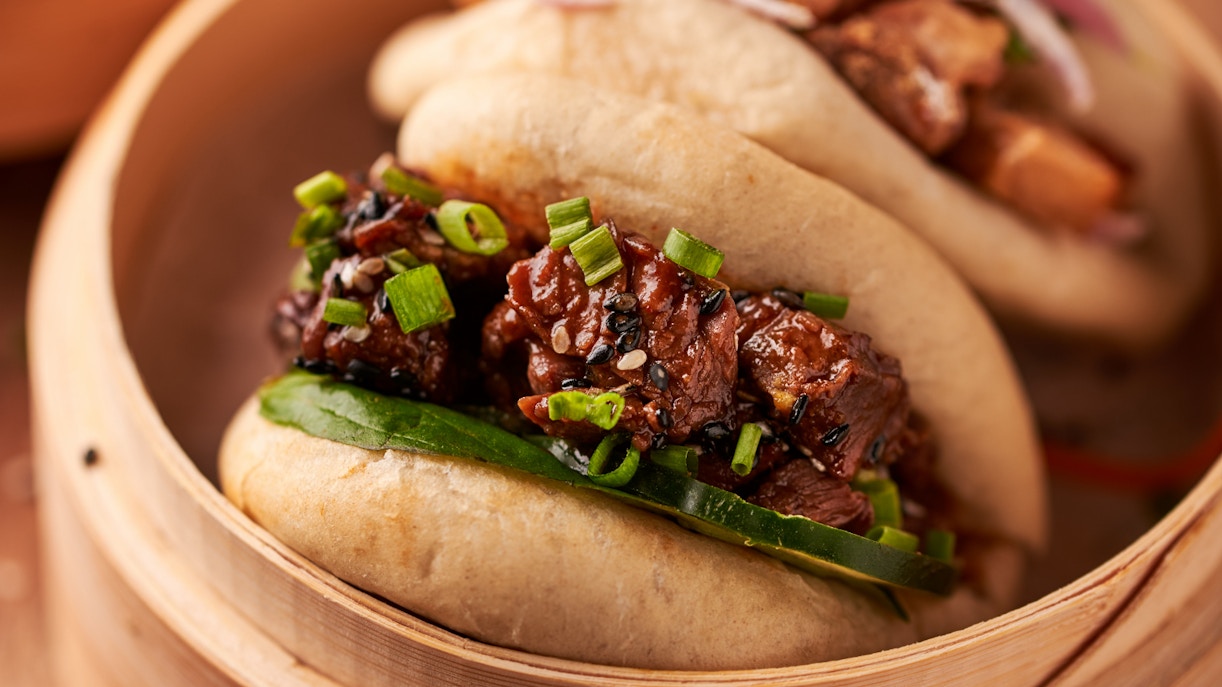 Pork bao with scallions and sesame seeds in a bamboo steamer.
