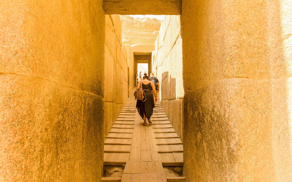 Visitors walking through ancient stone passageway at Giza Pyramids, Cairo.