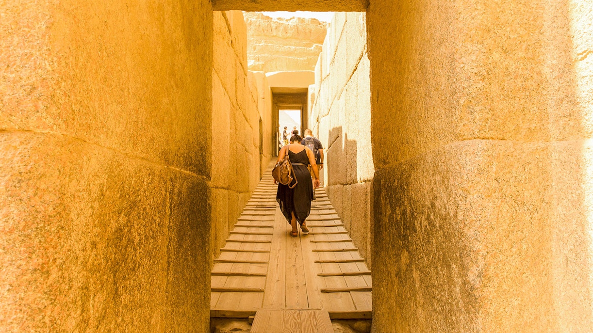 Visitors walking through ancient stone passageway at Giza Pyramids, Cairo.
