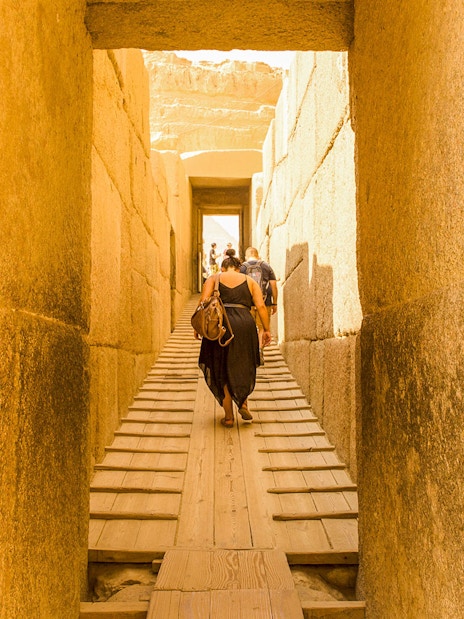 Visitors walking through ancient stone passageway at Giza Pyramids, Cairo.