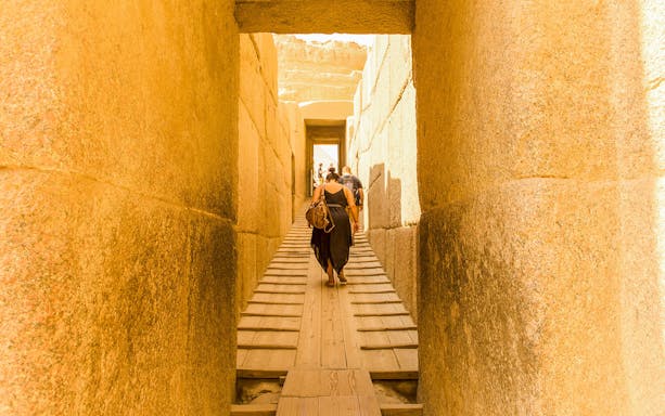 Visitors walking through ancient stone passageway at Giza Pyramids, Cairo.