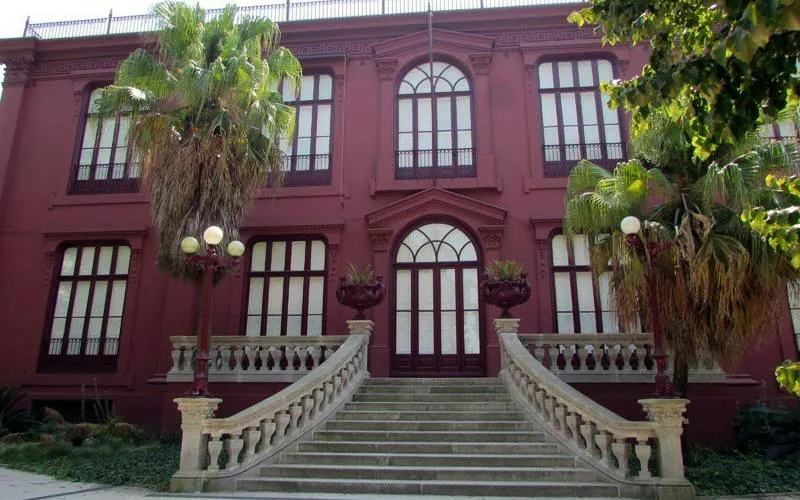 Elegant red building with arched windows and palm trees, Porto city exploration game.