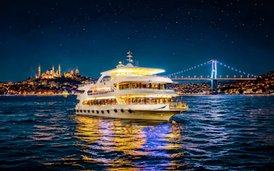 Cruise ship on Bosphorus strait at night with illuminated bridge and cityscape.