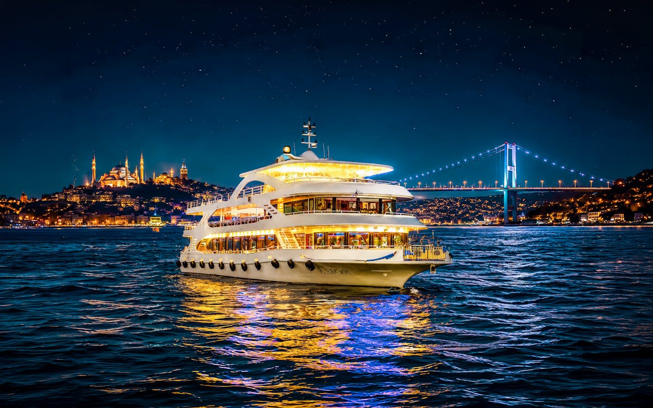 Cruise ship on Bosphorus strait at night with illuminated bridge and cityscape.
