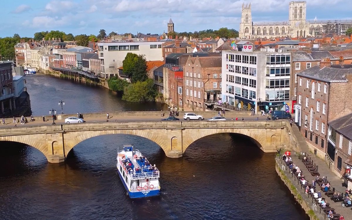 York sightseeing cruise passing under a historic stone bridge with York Minster in the background.