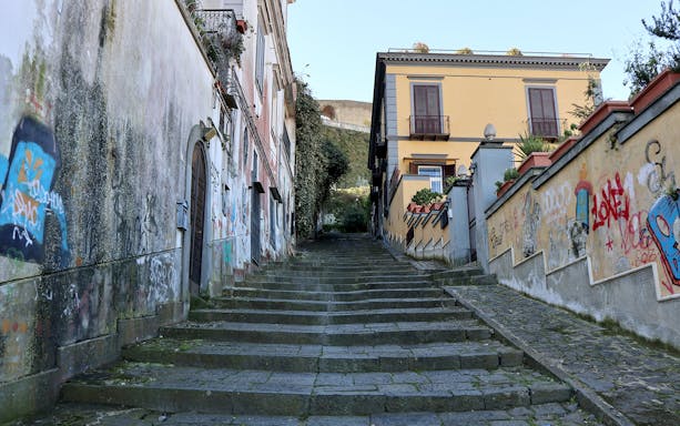 Stone steps of Pedamentina in Naples with graffiti-covered walls and historic buildings.