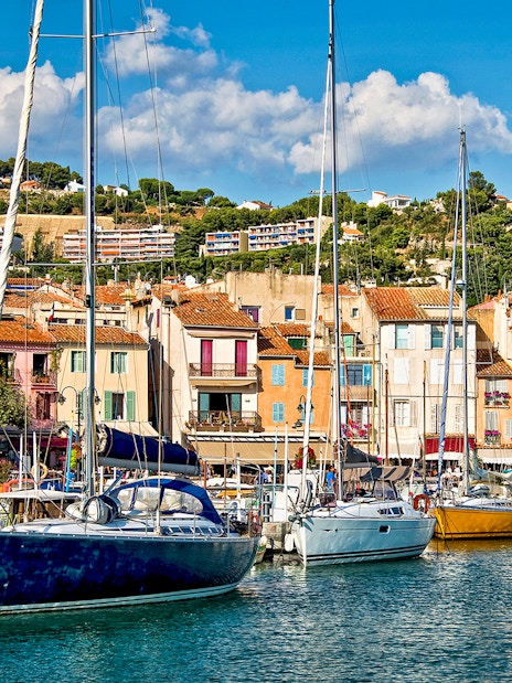 Boats docked at the colorful harbor of Cassis, France, with hillside buildings in the background.