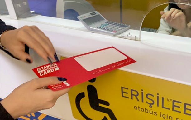 Hand holding Istanbul Welcome Card at Sabiha Gokcen Airport transfer desk.